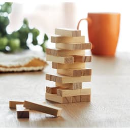A wooden Jenga tower with several blocks stacked and a few blocks scattered beside it, set on a table. An orange mug is in the background.