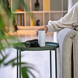 A drink bottle in white and black on a green table, with a hand resting on a grey sofa nearby.