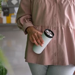 A drink bottle in white with a black lid, held by a person in a soft pink top.