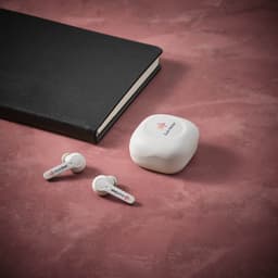 White earbuds with a charging case beside a black notebook on a textured pink background.