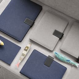 An assortment of folders in navy and grey with rPU closures, placed alongside decorative fish items.