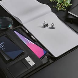 A black A4 folder with a notepad, phone, pen, and binder clips, featuring a zipper closure and additional pockets.