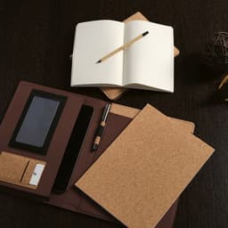 A cork A4 folder in brown, featuring a notepad, pen, and elastic closure, laid on a dark wooden surface.