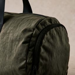 A green rNylon gym bag with a zippered pocket and black handles, showing textured fabric detail.