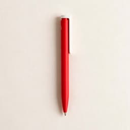 A red pen with a white clip rests against a light background. It features a sleek design and has a logo.