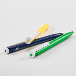 Three pens displayed: a blue pen, a green pen, and a yellow pen, each with a white cap and branding.