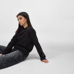 A black women's crew neck sweatshirt made from organic cotton and rPET, featuring a logo on the sleeve.