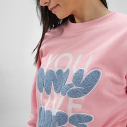 A pink women's crew neck sweatshirt made from organic cotton and rPET, featuring a textured design and a logo.
