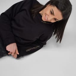 A women's crew neck sweatshirt in black, made from organic cotton and rPET, featuring a logo on the sleeve.