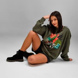 A green crew neck sweatshirt with floral design, paired with black shorts and boots. The model is sitting casually.