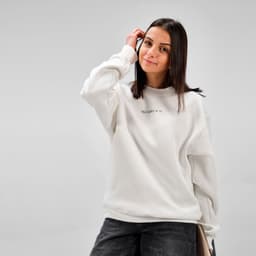 A white crew neck sweatshirt made of organic cotton and rPET, worn by a smiling woman with dark hair.