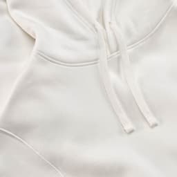 A white hooded sweatshirt with a textured surface and drawstrings. It features a logo and is made from organic cotton.