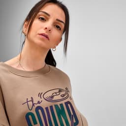A beige oversized sweatshirt with a graphic design and branding details, worn by a model with dark hair.