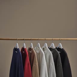 A rack displaying oversized sweatshirts in various colours: navy, red, brown, grey, black, and cream.