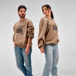 A beige oversized sweatshirt featuring a logo, worn by a man and a woman, styled with light blue jeans.