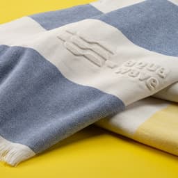 A cotton towel featuring a striped pattern in blue, white, and yellow, with a textured logo.