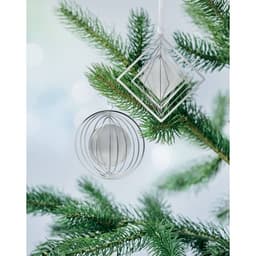 Two decorative ornaments hang from a pine tree branch, featuring geometric and circular shapes in silver.