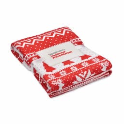 A red and white patterned blanket folded neatly, featuring Christmas-themed designs and a branded tag.
