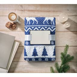 A blue and white patterned blanket lies on a wooden surface, alongside a cup of coffee, cookies, and candles.