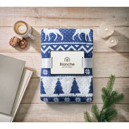 A folded blue and white blanket featuring a festive pattern, placed on a wooden surface with cookies and a cup of coffee.