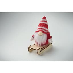 A decorative gnome in a red and white striped hat sits on a wooden sleigh. The gnome has a fluffy white beard.