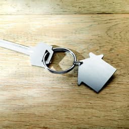 A silver key with a house-shaped keyring rests on a wooden surface.