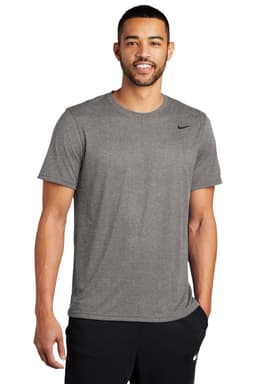 A man wearing a grey Nike T-shirt stands smiling, with a logo on the chest and black pants.