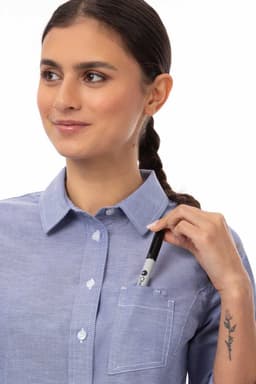 A woman wearing a light blue classic shirt with a pocket, holding a pen near the collar.