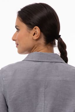 A woman with a ponytail wearing a grey Oxford shirt, viewed from the back, showcasing the collar and fabric texture.