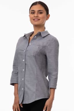 A grey women's classic shirt featuring a collar, button closure, and three-quarter sleeves. It has a logo detail.