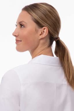 A woman in a white modern Oxford shirt, looking over her shoulder with her hair in a ponytail. The shirt features a logo.