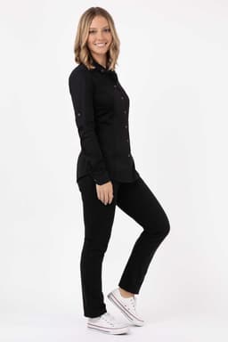 A woman in a black Seville shirt poses against a plain background, paired with black pants and white sneakers.