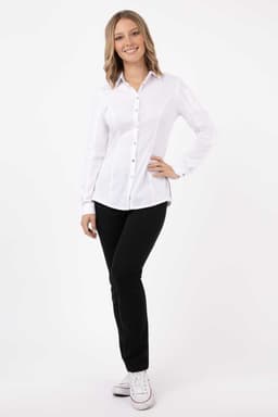 A woman wearing a white button-up shirt paired with black trousers and sneakers, standing in a relaxed pose.