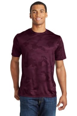 A maroon Sport-Tek CamoHex Tee featuring a camouflage pattern, worn by a smiling male model. The shirt has a logo.