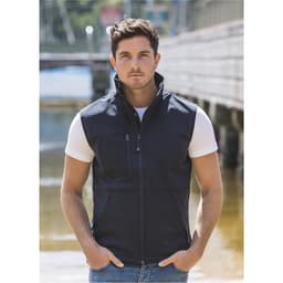 A black softshell vest with a zip front, featuring pockets and a high collar, worn by a man by the water.
