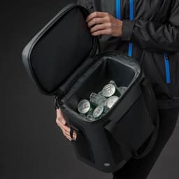 A black cooler bag with a zippered lid, filled with drink cans and ice, held by a person wearing a jacket.