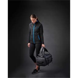 A black duffel bag with blue accents, held by a person wearing a black jacket and leggings.