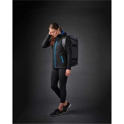 A woman in a black jacket with blue accents and leggings, carrying a duffel bag on her back.