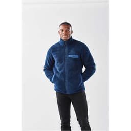 A navy blue men's Bergen Sherpa fleece jacket with a zip front and a pocket. The model is standing with hands in pockets.