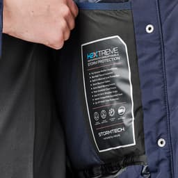 A navy puffer jacket featuring an interior label detailing storm protection and comfort features, with a logo present.