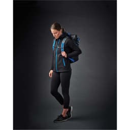A woman in a black hoodie with blue accents, wearing black leggings and a backpack, stands against a dark background.
