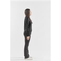 A side view of a woman wearing a black long-sleeve crew neck shirt and black pants, standing on a plain background.