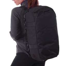 A black duffle bag is being worn on the back of a person in a grey jacket. The bag features a logo.