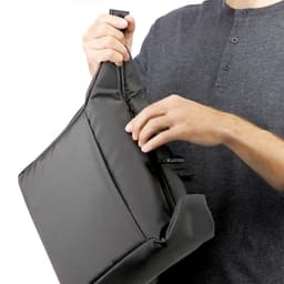 A person holding a dark grey cooler bag with a zippered opening and a shoulder strap.