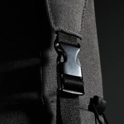 A close-up of a black duffle bag strap featuring a plastic clip fastener and textured fabric.