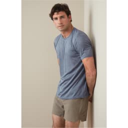 A man is wearing a blue recycled sports T-shirt, standing against a light wall, paired with beige shorts.