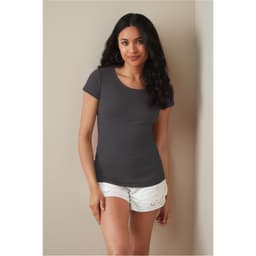 A woman wearing a grey crew neck t-shirt paired with white shorts, standing against a neutral background.