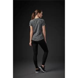 A woman is wearing a grey patterned short-sleeve T-shirt, paired with black leggings and sneakers. The back view is displayed.