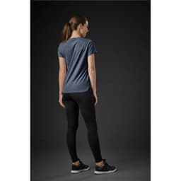 A woman wearing a navy blue crew neck tee paired with black leggings, standing against a dark background.