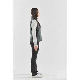 A side view of a women's fleece vest in dark grey, worn over a light long-sleeve top, with zipped pockets.